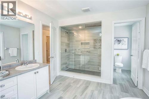 Spa-inspired primary bathroom featuring a frameless glass-enclosed walk-in shower with linear floor drain, dual vanity with white cabinetry and integrated sink, wood-finish plank flooring, and abundan - 525 Red Elm Road, Shelburne, ON - Indoor Photo Showing Bathroom
