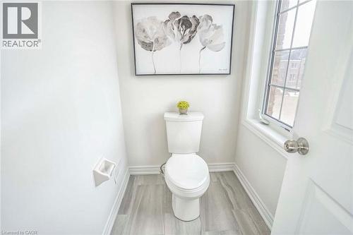 White toilet, wood-finish flooring, white trim, and a window with grid patterns - 525 Red Elm Road, Shelburne, ON - Indoor Photo Showing Bathroom