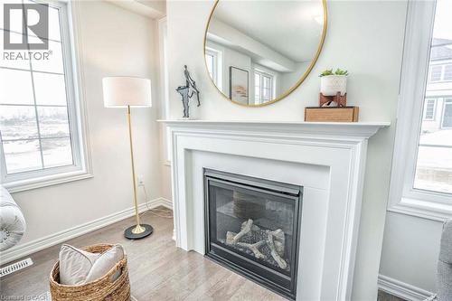 Bright living room anchored by a gas fireplace with surround molding and black metal frame insert, topped with a round brass-framed mirror and wooden mantel shelf - 525 Red Elm Road, Shelburne, ON - Indoor Photo Showing Living Room With Fireplace