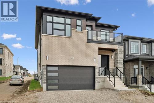 Modern exterior with light brick and stone accents, a glass-paneled balcony, a dark garage door with horizontal windows, and contemporary black-framed windows - 451 Benninger Street, Kitchener, ON 