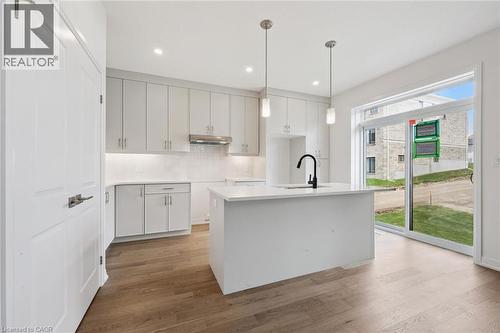 Modern kitchen featuring light-toned cabinetry, a central island with a sink, two pendant lights, wood-finish flooring, and a sliding glass door - 451 Benninger Street, Kitchener, ON 