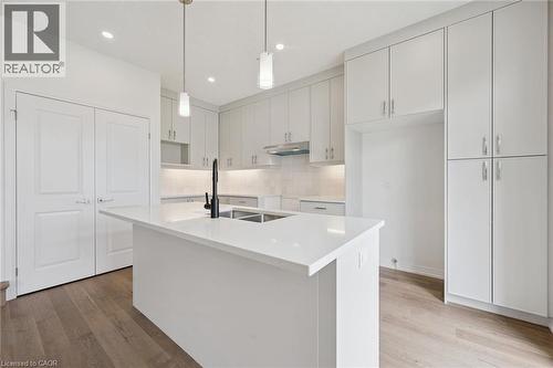 Kitchen featuring wood-finish flooring, white cabinetry, a central island with an integrated sink, white countertops, and recessed lighting - 451 Benninger Street, Kitchener, ON 