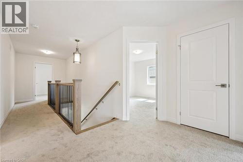 Carpeted hallway with a wood and metal baluster staircase, a paneled interior door, and a pendant light fixture - 451 Benninger Street, Kitchener, ON 
