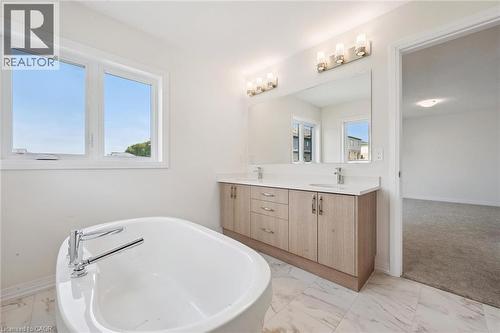 Freestanding soaking tub with chrome fixtures, dual sink vanity with stone countertop, large wall-mounted mirror, and tile flooring - 451 Benninger Street, Kitchener, ON 