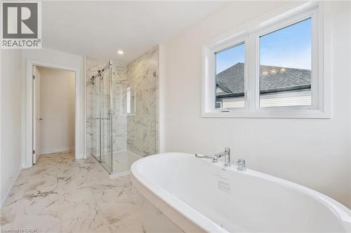 Freestanding soaking tub with chrome fixtures, glass-enclosed shower with marble-finish tile, and large window with white trim - 451 Benninger Street, Kitchener, ON 
