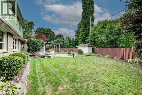 Spacious backyard featuring a manicured lawn, stone patio with pergola, privacy fencing, mature landscaping, and an outdoor storage shed - 97 Somerset Crescent, Waterloo, ON - Outdoor