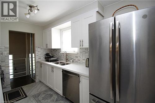 White cabinetry, stainless steel appliances, mosaic tile backsplash, double basin sink, and recessed lighting - 35 Garden Crescent, Hamilton, ON - Indoor Photo Showing Kitchen With Double Sink