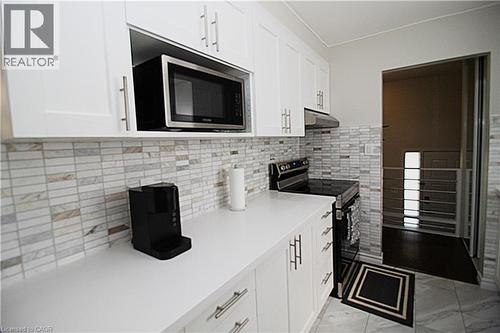White shaker-style cabinetry, a built-in microwave, stone-finish backsplash, smooth cooktop range, and light-toned countertops - 35 Garden Crescent, Hamilton, ON - Indoor Photo Showing Kitchen