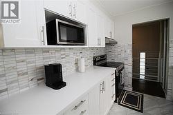 White shaker-style cabinetry, a built-in microwave, stone-finish backsplash, smooth cooktop range, and light-toned countertops - 