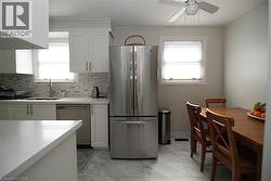 White cabinetry, tile backsplash, stainless steel appliances, white countertops, and tile flooring - 