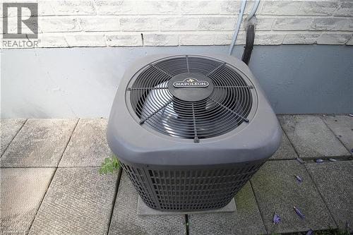 Exterior HVAC unit on a concrete paver base, set against a painted brick wall - 35 Garden Crescent, Hamilton, ON - 