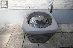 Exterior HVAC unit on a concrete paver base, set against a painted brick wall - 