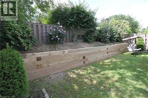 Manicured lawn with a wood retaining wall, established plantings, and a privacy fence - 35 Garden Crescent, Hamilton, ON - Outdoor