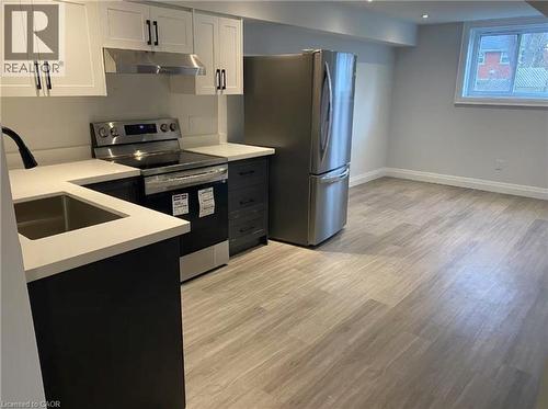 Modern kitchen featuring stainless steel appliances, white upper cabinetry, dark lower cabinetry, light-toned countertops, and wood-finish flooring - 81 Second Avenue Unit# B, Kitchener, ON - Indoor Photo Showing Kitchen