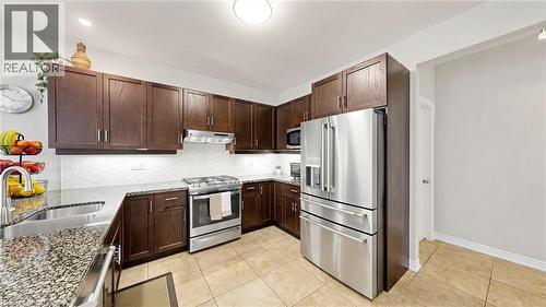 Kitchen featuring wood-finish cabinetry, granite-style countertops, stainless steel appliances, a tile backsplash, and tile flooring - 173 Raymond Road, Ancaster, ON - Indoor Photo Showing Kitchen With Stainless Steel Kitchen With Double Sink With Upgraded Kitchen