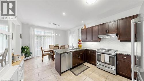 Kitchen featuring dark wood cabinetry, stainless steel appliances, light-toned hexagon tile backsplash, and light-toned granite countertops - 173 Raymond Road, Ancaster, ON - Indoor Photo Showing Kitchen With Stainless Steel Kitchen With Double Sink