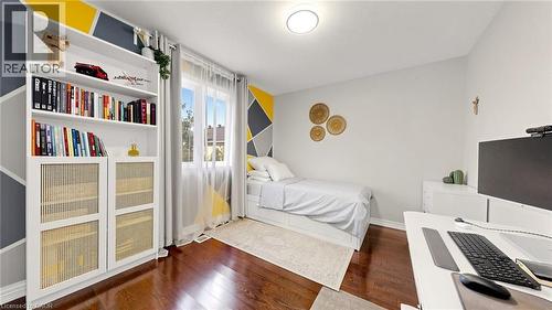 Rich wood-finish flooring, built-in shelving, window with sheer and blackout curtains, and a ceiling-mounted light fixture - 173 Raymond Road, Ancaster, ON - Indoor Photo Showing Bedroom
