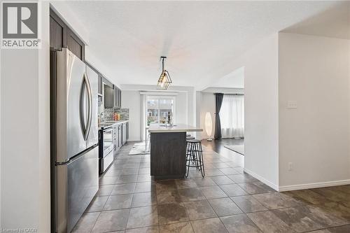 Modern kitchen featuring stainless steel appliances, dark wood-finish cabinetry, a large center island with light-toned countertop, and a geometric pendant light fixture - 360 Freure Drive, Cambridge, ON - Indoor