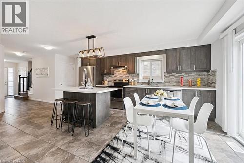 Modern kitchen featuring dark wood-finish cabinetry, stainless steel appliances, a center island with seating, and a tile backsplash - 360 Freure Drive, Cambridge, ON - Indoor Photo Showing Dining Room