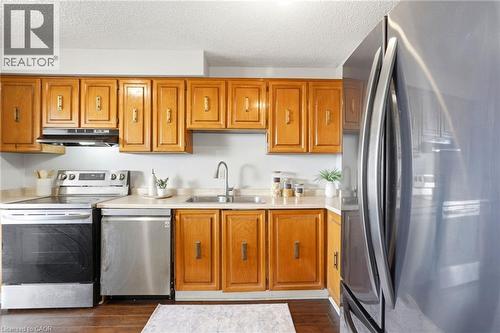 Kitchen featuring wood cabinetry, light-toned countertops, stainless steel appliances, and wood-finish flooring - 375 King Street N Unit# 708, Waterloo, ON - Indoor Photo Showing Kitchen With Double Sink