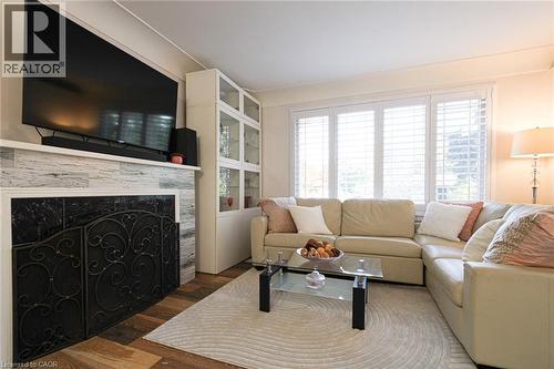 Wood-finish flooring, fireplace with stone surround, custom built-in cabinetry, and white window shutters - 2105 Maplewood Drive, Burlington, ON - Indoor Photo Showing Living Room With Fireplace
