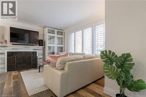Wood-finish flooring, fireplace with stone surround and ornamental screen, built-in display cabinetry, and window shutters - 2105 Maplewood Drive, Burlington, ON - Indoor Photo Showing Living Room With Fireplace