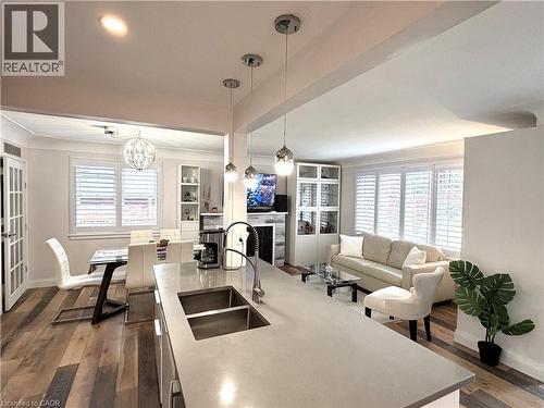 Kitchen island with integrated double sink, contemporary pendant lighting, wood-finish flooring, plantation shutters, and built-in shelving - 2105 Maplewood Drive, Burlington, ON - Indoor