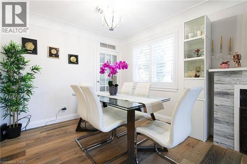 Wood-finish flooring, white wall paint, window with white louvered shutters, glass-front display cabinetry, and a decorative fireplace surround - 2105 Maplewood Drive, Burlington, ON - Indoor Photo Showing Dining Room