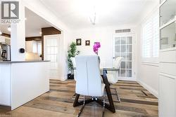 Wood-finish flooring throughout, white plantation shutters, white built-in cabinetry with glass fronts, and a white paneled door with glass inserts - 