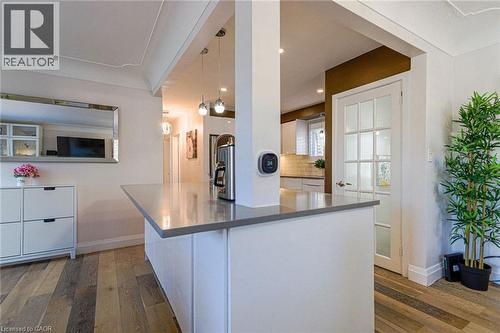 Wood-finish flooring, white paneled cabinetry, pendant lighting, built-in counter space, and a glass-paneled door - 2105 Maplewood Drive, Burlington, ON - Indoor Photo Showing Kitchen