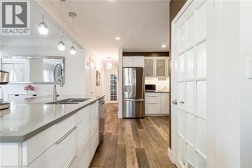 Kitchen featuring a large island with an undermount sink, stainless steel appliances, white cabinetry, and wood-finish flooring - 2105 Maplewood Drive, Burlington, ON - Indoor Photo Showing Kitchen With Stainless Steel Kitchen With Double Sink With Upgraded Kitchen