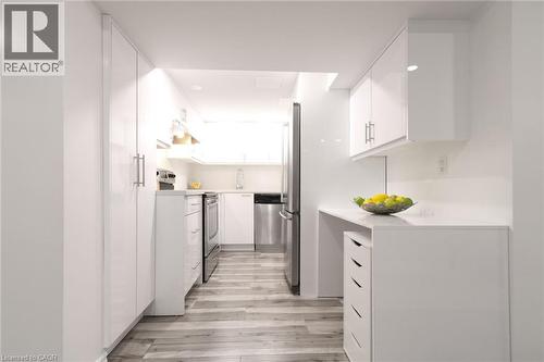 Galley kitchen featuring white cabinetry, stainless steel appliances, light-toned wood-finish flooring, and recessed lighting - 2105 Maplewood Drive, Burlington, ON - Indoor