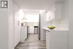 Galley kitchen featuring white cabinetry, stainless steel appliances, light-toned wood-finish flooring, and recessed lighting - 