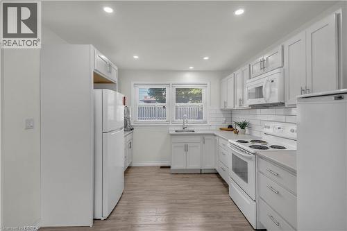 Bright kitchen featuring white cabinetry, subway tile backsplash, light-toned countertops, and wood-finish flooring - 450 Highland Road E, Kitchener, ON - Indoor Photo Showing Kitchen