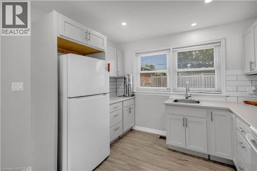 Modern kitchen featuring light gray cabinetry, light countertops, wood-finish flooring, white subway tile backsplash, and a double window with blinds - 450 Highland Road E, Kitchener, ON - Indoor Photo Showing Kitchen
