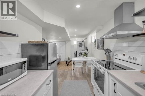 Open-concept living space featuring a full kitchen with stainless steel appliances, a stackable washer and dryer, recessed lighting, and wood-finish flooring - 450 Highland Road E, Kitchener, ON - Indoor Photo Showing Kitchen