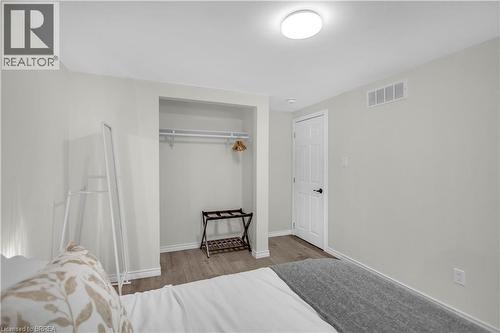 Bedroom featuring wood-finish flooring, recessed closet with hanging rod, white door with black hardware, white baseboards, and a flush-mount ceiling light fixture - 450 Highland Road E, Kitchener, ON - Indoor Photo Showing Bedroom