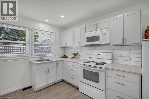 Bright kitchen featuring white shaker cabinetry, light-toned countertops, subway tile backsplash, stainless steel sink with a gooseneck faucet, and wood-finish flooring - 450 Highland Road E, Kitchener, ON - Indoor Photo Showing Kitchen
