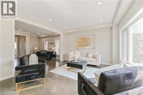 Sophisticated open-concept living space featuring recessed ceiling lighting, large windows with natural light, wood-finish flooring throughout, and a black leather accent chair with brass-finished fra - 24 Weatherall Avenue, Cambridge, ON - Indoor Photo Showing Living Room