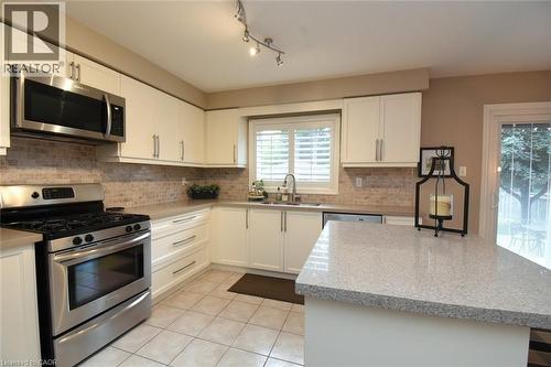 White cabinetry with brushed nickel hardware, stainless steel appliances, tiled backsplash, light-colored countertops, and an eat-at island - 470 Amanda Crescent, Burlington, ON - Indoor Photo Showing Kitchen With Double Sink