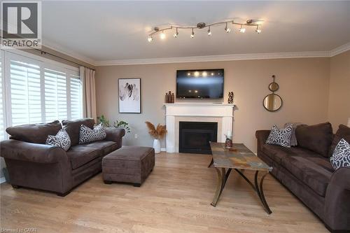 Wood-finish flooring, crown molding, fireplace with white mantel, white window shutters, and track lighting - 470 Amanda Crescent, Burlington, ON - Indoor Photo Showing Living Room With Fireplace