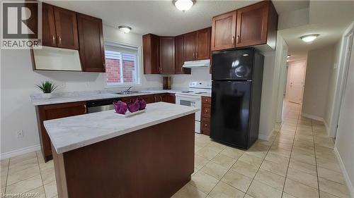 Spacious kitchen featuring rich wood cabinetry, a large center island with white countertop, stainless steel appliances including refrigerator and range, tile flooring, and abundant natural light from - 128 Udvari Crescent Unit# A, Kitchener, ON - Indoor Photo Showing Kitchen With Double Sink