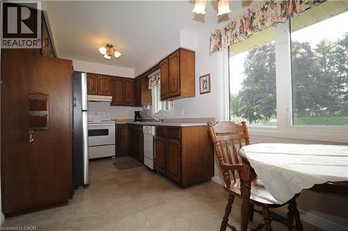 Kitchen featuring wood-finish cabinetry, white appliances, and a large window overlooking mature trees - 14 Berkley Crescent, Simcoe, ON - Indoor