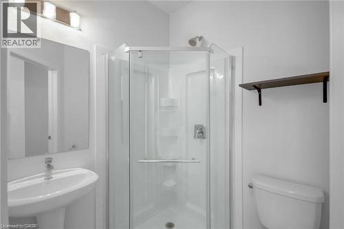 White pedestal sink with a chrome faucet, mirrored vanity, glass-enclosed shower, white toilet, and a wall-mounted wood-finish shelf - 961 Battery Park, London, ON - Indoor Photo Showing Bathroom