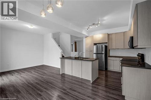 Open-concept living area featuring wood-finish flooring, a kitchen island with integrated sink, stainless steel refrigerator, light-toned cabinetry, and dark countertops - 961 Battery Park, London, ON - Indoor Photo Showing Kitchen