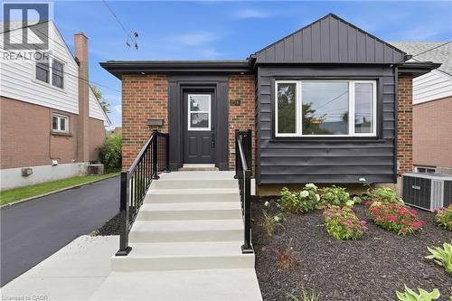 Brick facade with black siding accents, modern black front door, concrete steps with black railings, landscaped garden bed with mulch, paved driveway - 156 East 36Th Street, Hamilton, ON - Outdoor