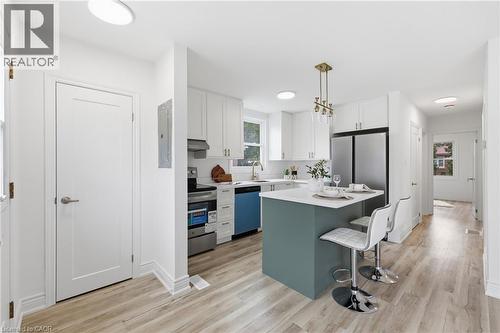 Open-concept kitchen featuring an island with a breakfast bar, stainless steel appliances, white cabinetry, and wood-finish flooring - 156 East 36Th Street, Hamilton, ON - Indoor Photo Showing Kitchen With Upgraded Kitchen