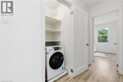 White front-load washer, built-in shelving, white paneled interior doors, and wood-finish flooring - 156 East 36Th Street, Hamilton, ON - Indoor Photo Showing Laundry Room