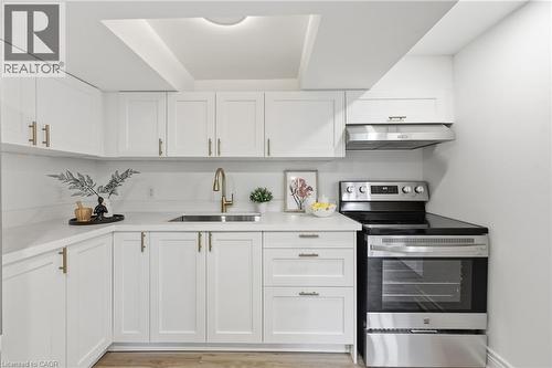White shaker-style cabinetry, stainless steel appliances, light-toned countertops, wood-finish flooring, and a gold-tone faucet - 156 East 36Th Street, Hamilton, ON - Indoor Photo Showing Kitchen With Upgraded Kitchen