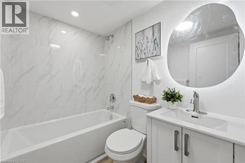 White tile surround with subtle veining, recessed lighting, built-in bathtub, white vanity with integrated sink, and illuminated oval mirror - 156 East 36Th Street, Hamilton, ON - Indoor Photo Showing Bathroom